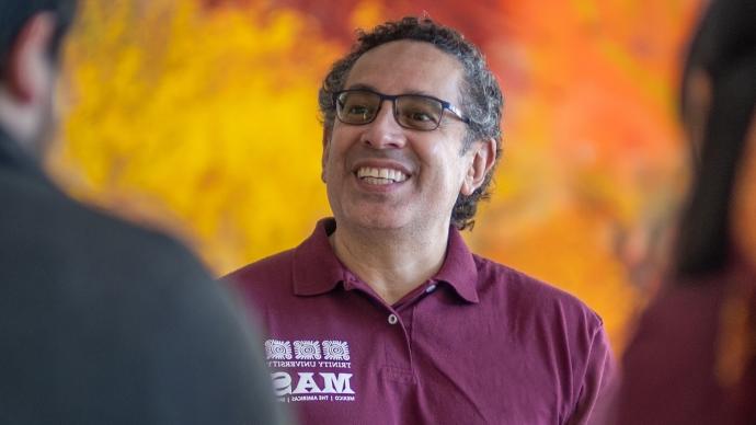 juan sepulveda smiles at two students with bright colored art in the background