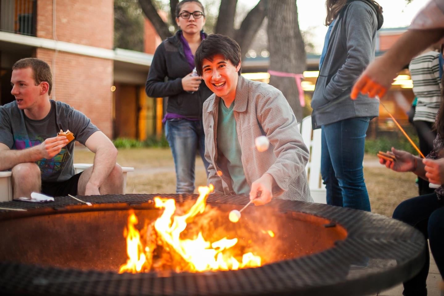 Group of students roasting marshmallows in an open pit