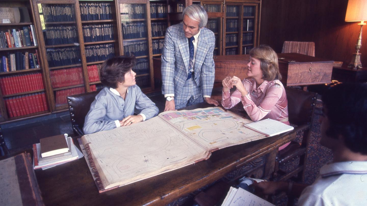 A man standing talking with two women while looking at a map of Trinity's campus.