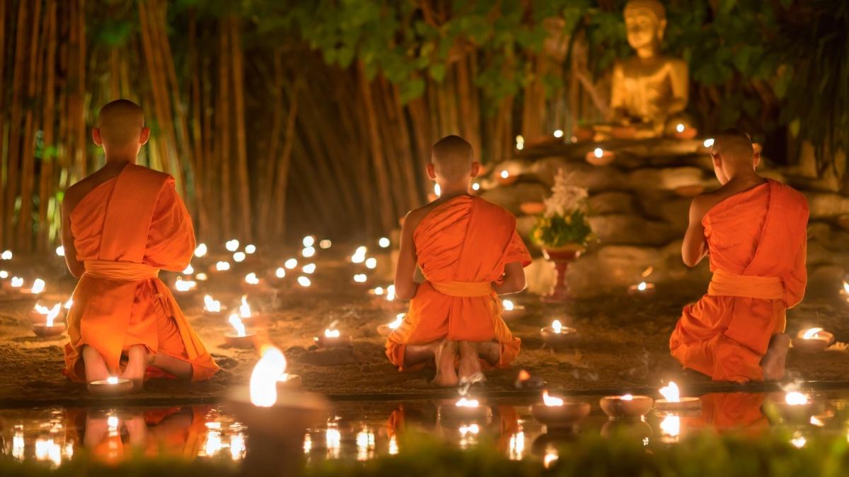 Buddhists kneeling in the dark surrounded by candles with a statue of the Buddha in the background