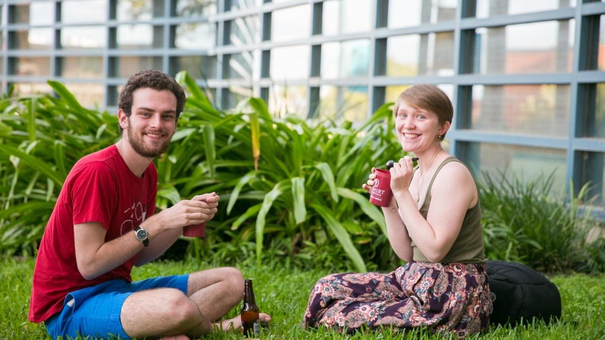 两个学生坐在草地上吃着用栗色杯子盛的冰淇淋